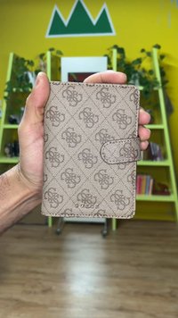 Brun mønstret pung med en tekstureret finish, med en tryknaplukning og præget "Guess"-logo nederst.