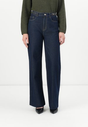 Dark blue wide-leg denim jeans with gold hardware accents, high waist, and contrast stitching, paired with a green ribbed sweater.