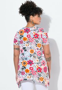 Túnica de manga corta con estampado floral en blanco, que presenta vibrantes flores en rosa, naranja y negro, con un dobladillo curvado y una tela suave y ligera.