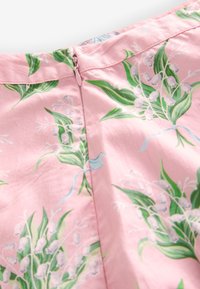 Material roz cu imprimeu floral de frunze verzi și flori albe în formă de clopoțel, având o închidere ascunsă cu fermoar roz.
