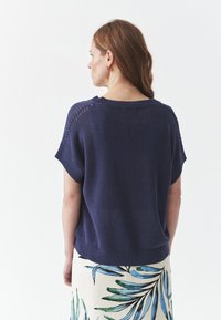 Top corto a maniche corte di colore blu navy con scollo ampio e dettagli di cucitura decorativa sulle spalle, abbinato a una gonna con motivo floreale.
