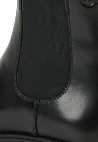 Gros plan d'une botte Chelsea en cuir noir montrant un panneau latéral élastique, une texture lisse et des détails de couture.