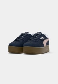 Pair of navy blue Puma Palermo sneakers with pink stripe and thick brown sole, shown from front side angle on white background.