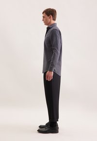 Camicia da uomo a maniche lunghe di colore blu scuro, con un delicato motivo a quadri, abbinata a pantaloni neri su misura e scarpe eleganti nere.