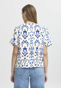 Top a maniche corte color crema con motivi astratti blu e navy. Realizzato in tessuto testurizzato con una vestibilità leggermente ampia e scollo rotondo.