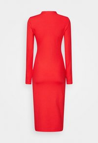 Röd rippad midikjol med långa ärmar och hög krage. Har en figurnära silhuett och en mjuk textur.