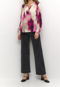 Blouse à manches longues, à motifs roses et beiges avec un col en V, associée à un jean noir taille haute à jambes larges et des chaussures noires à talons carrés.