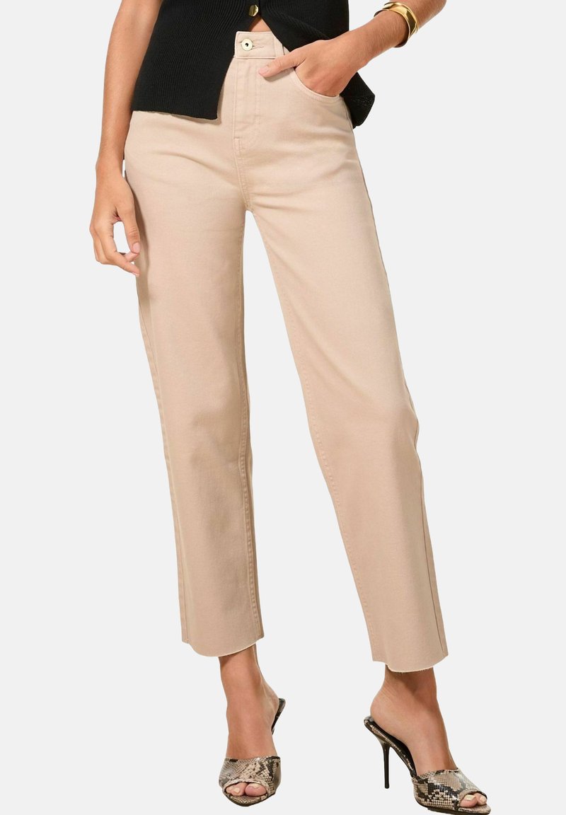 Pantalon beige à jambe droite avec taille haute, poches avant et fermeture à bouton, associé à des escarpins en imprimé serpent et un haut noir.