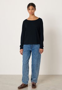 Svart långärmad topp med vid rund halsringning, kombinerad med ljusblå höga jeans och bruna båtskor; slät textur och avslappnad passform.