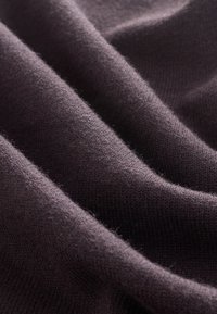 Mørkelilla strikket stof med blød tekstur, der indeholder blide folder og bølger, som fremhæver dets fleksibilitet og varme.