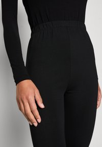 Leggings noirs avec taille élastique, fabriqués dans un tissu lisse et extensible. Design ajusté dans une couleur unie, mettant en valeur une silhouette épurée.