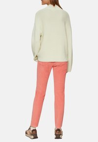 Jasnożółty, prążkowany sweter z wysokim kołnierzem i opuszczonymi ramionami, w połączeniu z różowymi spodniami z korduuru i trampkami z brązowymi akcentami.