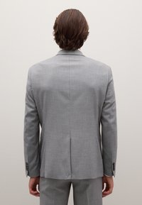 Lichtgrijs colbert met een gestructureerde afwerking. Heeft een enkele achterkantsplit, revers met insnijding en aan de knoopjes gesloten manchetten. Getailleerde pasvorm, minimalistisch ontwerp.