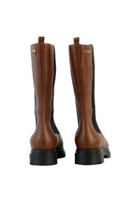 Botas de cuero marrón hasta la rodilla con paneles laterales elásticos negros y suelas gruesas negras, vistas desde atrás sobre un fondo blanco.