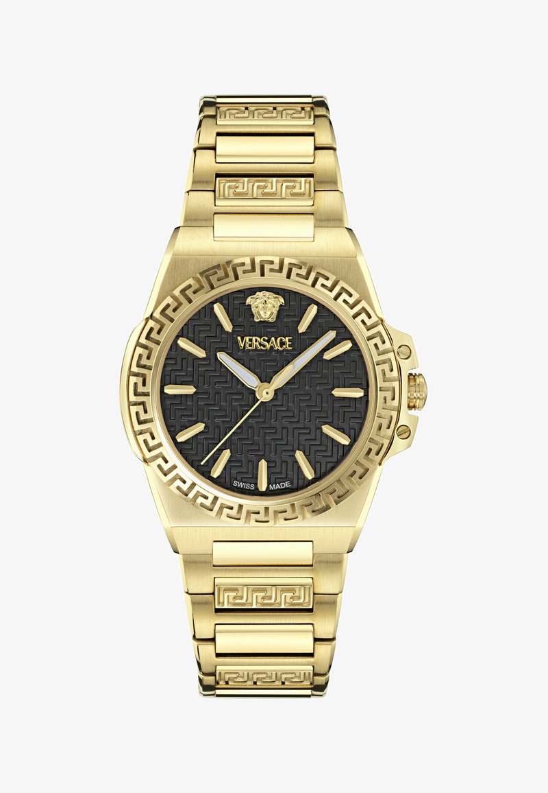 Arany tónusú óra fekete mintás számlappal. A jellemzők között szerepel egy texturált perem, görög kulcs minta a karkötőn, valamint arany órás jelzők és mutatók.