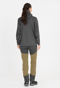 Harmaa pitkähihaine paita, jossa on korkea kaulus, yhdistettynä väriblokkihousuihin: tummaa harmaata ja oliivinvihreää, joissa on säädettävät hihansuut ja mustat saappaat.