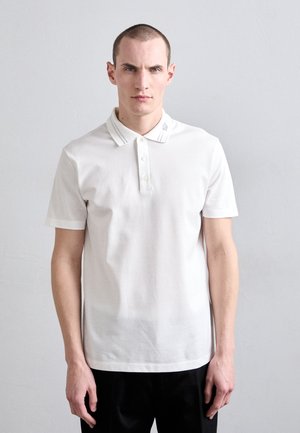 White polo shirt with short sleeves, three buttons, and a collar. Features subtle logo detail on the collar. Smooth fabric texture.