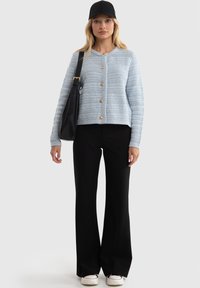 Gaiši zils tekstūrēts adīts kardigāns ar apaļu kaklu, sešām zelta pogām, kopā ar melnām platām biksēm un melnu cepuri. Melnā soma uz pleca.