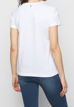 Hvid t-shirt i bomuld med korte ærmer, rund halsudskæring og et lille broderet detaljer på ryggen. Kombineret med blå denimjeans.