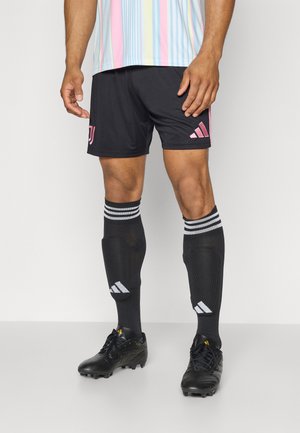 Shorts de sport noirs avec des accents et un logo roses, associés à des chaussettes noires avec des rayures blanches et des crampons noirs. Texture lisse, design sportif.