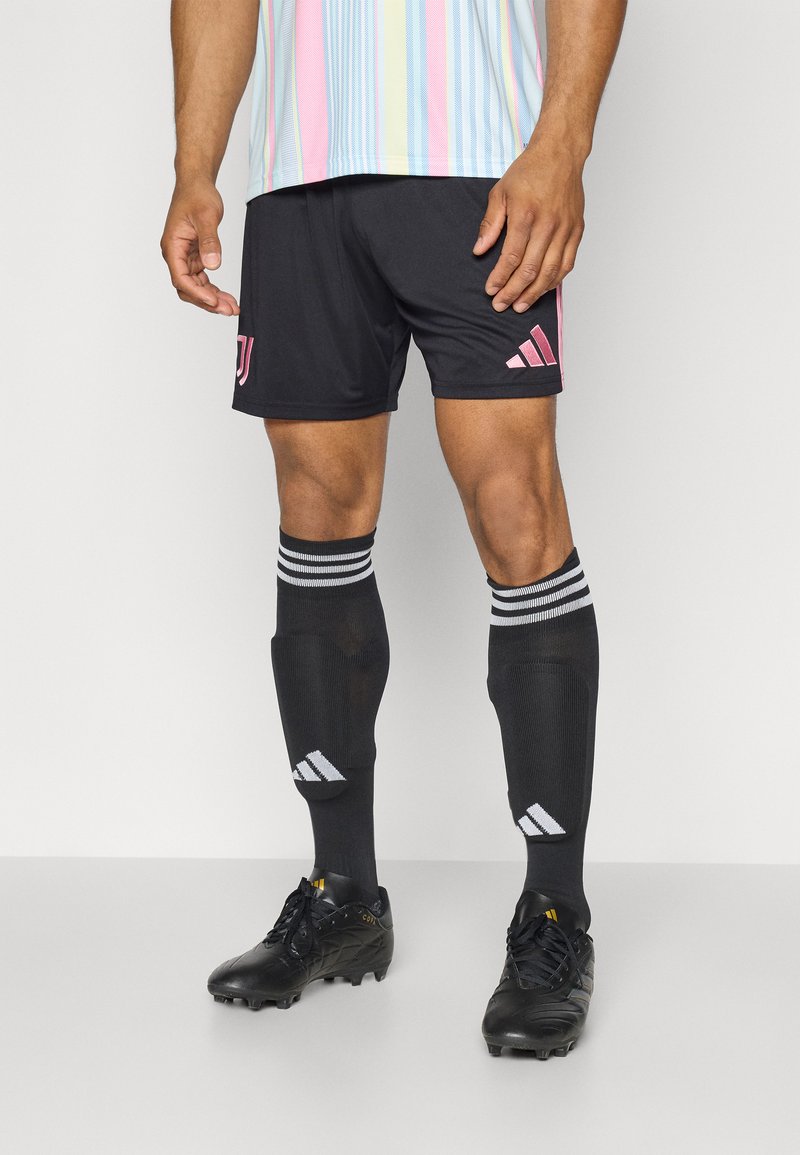 Czarne spodenki sportowe z różowymi akcentami i logo, w połączeniu z czarnymi skarpetami z białymi paskami i czarnymi butami do biegania. Gładka faktura, sportowy design.