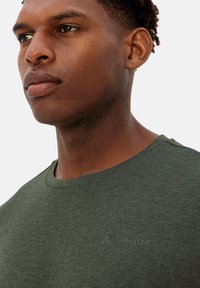 T-shirt verde a girocollo realizzata in tessuto testurizzato, con un logo discreto sul petto, vista ravvicinata che mette in evidenza il collo e il motivo.