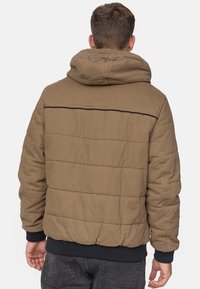 Braune, gepolsterte Jacke mit Kapuze, die ein gesteppter Design und gerippte Säume aufweist, von hinten gezeigt. Mit einer schwarzen Naht über den Schultern akzentuiert.