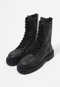 Para czarnych skórzanych, sznurowanych butów wojskowych z bocznymi zamkami i wytrzymałymi, grubymi podeszwami na białym tle.