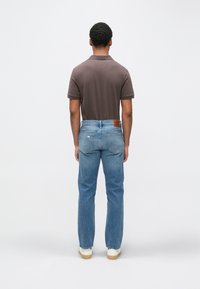 Hnedé polokošeľa, modré džíny s rovnými nohavicami a biele topánky. Džíny majú zadnú záplatu a jemné vyblednutie; košeľa má klasický golier.