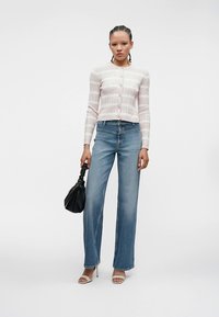 Cardigã às riscas em rosa claro, com botões à frente, combinado com jeans azuis de cintura alta. Acessórios incluem uma mala preta e saltos de cor clara.