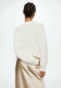 White knitted sweater with a textured finish, featuring long sleeves and a relaxed fit, paired with a satin beige skirt.