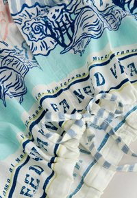 Světle modrá a bílá látka s modrými vzory mušlí, tmavě modrý text a bílý a modrý proužkovaný stahovací šňůrka na zavazování.