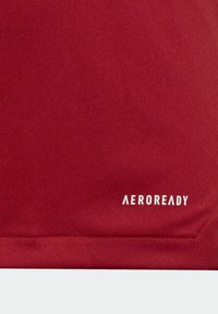 Acercamiento del tejido rojo con el logo bordado en blanco "AEROREADY" cerca de la esquina inferior derecha.