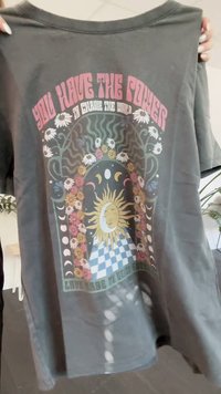 T-shirt de algodão cinza com um design gráfico vibrante, apresentando sol e lua, padrões florais e elementos psicadélicos em rosa, amarelo e verde.