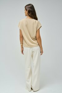 Top corto de manga corta de color beige, elaborado con una tela suave, combinado con pantalones de pierna ancha blancos. Diseño simple, textura suave, sin patrones ni detalles.