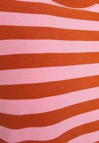 Horizontální střídající se pruhy textilie růžové a rezavé barvy vytvářející detailní pohled na pletený textilní povrch.