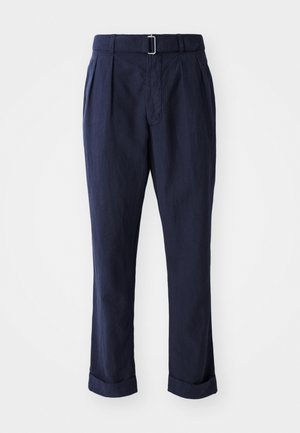 Pantalones azul marino hechos de tejido ligero, con un cinturón de hebilla plateada, pliegues en la parte frontal y puños enrollados en los tobillos.