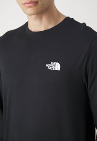 Černé tričko s dlouhým rukávem vyrobené z bavlny s kulatým výstřihem. Na levé straně hrudi je malé bílé logo "The North Face".