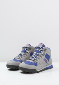 Chaussures de randonnée en suède gris et tissu bleu avec un design montante, dotées d'une semelle robuste, de lacets gris et d'œillets métalliques.