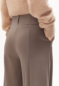 Graue Hosen im maßgeschneiderten Schnitt mit glatter Textur, seitlichen Taschen und einer Gesäßtasche, kombiniert mit einem leichten Strickpullover.