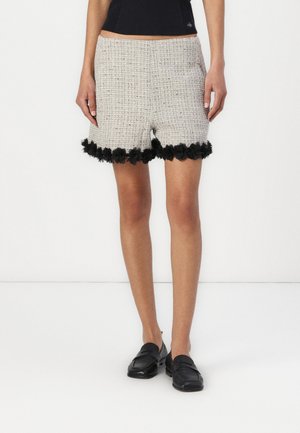 Kahvipohjaiset tweed-shortsit, joissa on teksturoitu kuvio, ja musta kukkakoristelu helman ympärillä. Yhdistetty mustiin loafer-kengiin.