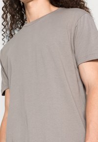 Grijze T-shirt met korte mouwen, gemaakt van zachte stof; heeft een ronde halslijn en een relaxed fit, met zichtbare stikdetails langs de naden.