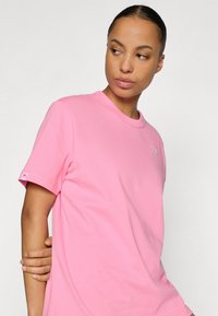 Ružové bavlnené tričko s okrúhlym výstrihom a krátkymi rukávmi, s malým logom na hrudi a štítkom na manžete. Mäkká textúra.