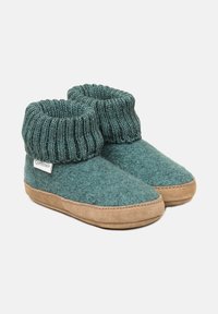 Pantofole in lana morbida color teal con risvolti a costine spessi e suole in suede color nocciola, posizionate affiancate su uno sfondo bianco.
