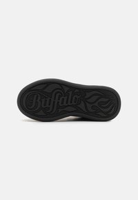 Svart gummisula till sneaker med präglad "Buffalo"-logotyp och virvlande flamdesign. Strukturerad yta med rundade kanter.