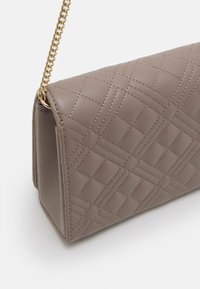 Přešívaná kabelka přes rameno v světle taupe barvě z umělé kůže. Řetízkový popruh s kulatými hranami a kontrastním prošíváním, obdélníkového tvaru.