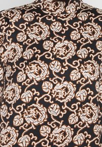Tela negra con un intrincado patrón floral en blanco y óxido, con enredaderas en espiral y acentos detallados. Diseño de alto cuello.