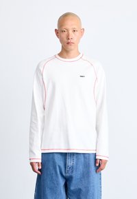 Long-sleeve white T-shirt with red contrast stitching and a small black "OBEY" logo on the chest. Soft fabric with a relaxed fit.