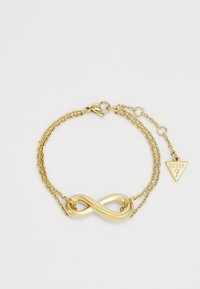Bracciale placcato in oro con simbolo dell'infinito, design a doppia catena e ciondolo triangolare con la scritta "GUESS" incisa.