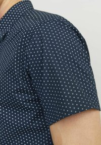 Camicia a maniche corte in tessuto blu scuro con un motivo geometrico di diamanti bianchi, dotata di colletto e cuciture curate lungo le maniche.
